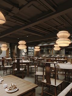 an empty restaurant with wooden tables and white plates on the table, lights hanging from the ceiling