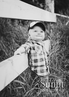 black and white photograph of a young boy leaning against a fence with his hat on