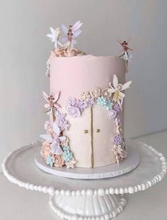 a pink cake with flowers and butterflies on top is sitting on a white platter