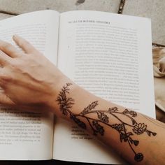 a woman's arm with flowers on it and an open book in the background