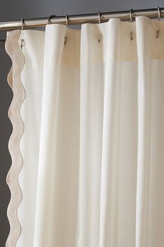 a white curtain hanging on the side of a metal rod with an embroidered lace edge