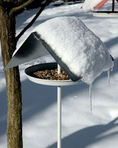 a bird feeder covered in snow next to a tree