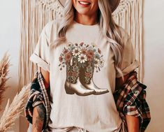 Combine cowgirl toughness with floral finesse in the "Blooming Boots" Tee from Lasso & Lace, printed on a soft Bella Canvas 3001 tee. Available in white, natural, soft cream, and soft pink, exclusively on Etsy. The "Blooming Boots" Tee is a celebration of the cowgirl's spirit, marrying the durable icon of cowboy boots with the delicate touch of springtime flowers. Lasso & Lace presents this exclusive design, offering a unique take on Western apparel. Screen printed on the popular Bella Canvas 30 Western Apparel, Western Tee, Western Graphic Tees, Cowgirl Chic, Soft Pink Color, Country Shirts, Cow Girl, Cow Boy, Western Shirt