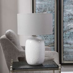 a white lamp sitting on top of a table next to a gray chair and ottoman