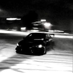 black and white photograph of a car driving down the road at night time with headlights on