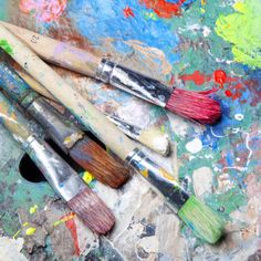 paintbrushes sitting on top of a table covered in lots of different colored paints