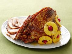 a white plate topped with meat and pineapple slices next to sliced bananas on a green table