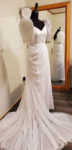 a white wedding dress on display in front of a mirror with mannequins