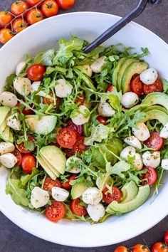 a salad with tomatoes, avocado and mozzarella on top in a white bowl