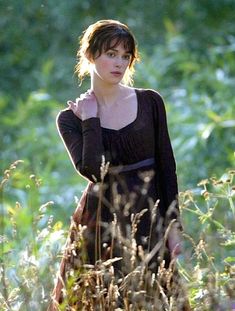 a woman standing in tall grass with her hand on her shoulder