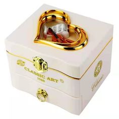 a white box with gold trimmings and a heart shaped ring in the middle