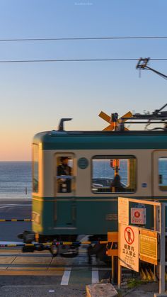 a green and white train traveling down tracks next to the ocean with power lines above it