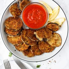 a white plate topped with fried food next to a bowl of sauce and a fork