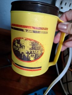 a person holding a yellow coffee cup on top of a wooden table next to an electrical outlet