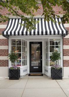 a black and white striped awning over the entrance to a store with potted plants