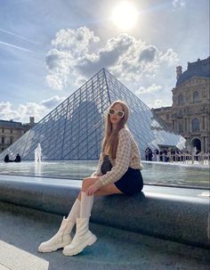 a woman sitting on the edge of a fountain in front of a building with a pyramid