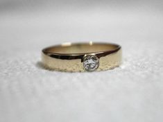 a gold wedding ring with a diamond on it sitting on a white tableclothed surface