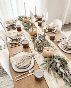 the table is set with white plates and silverware, pumpkins, greenery, and candlesticks