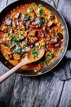 a pan filled with meat and vegetables on top of a wooden table next to a spoon