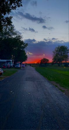 the sun is setting over an rv park with cars parked on the side of the road