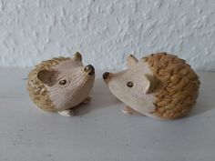 two hedgehog figurines sitting next to each other on a counter top in front of a white wall