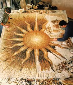 two men are working on a mosaic in the shape of a sun, surrounded by wood shavings