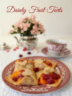 some fruit pastries are on a plate next to a tea cup and saucer