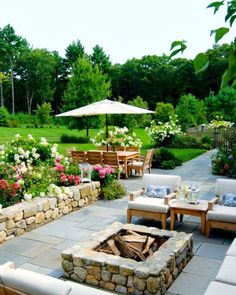 an outdoor patio with seating and fire pit surrounded by flowers, trees, and greenery