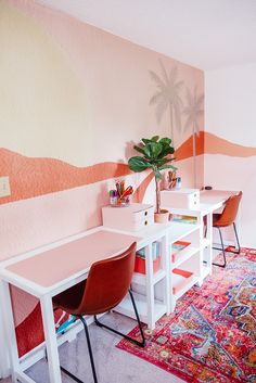 a desk with two chairs and a potted plant on it in front of a pink wall