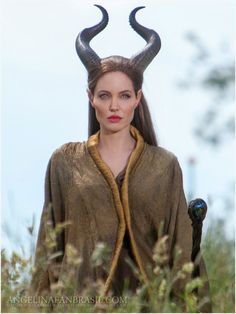 a woman with horns on her head standing in tall grass