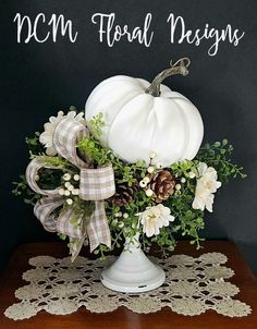 a white pumpkin sitting on top of a table with greenery and ribbon around it