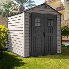 a small gray shed sitting on top of a lush green field next to a building