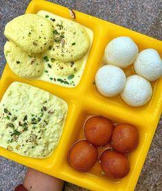 a yellow tray filled with different types of food on top of a table next to a person's hand