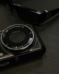 a black camera sitting on top of a table next to sunglasses and a cell phone