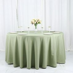 a round table with two vases and flowers on it, in front of a white curtain