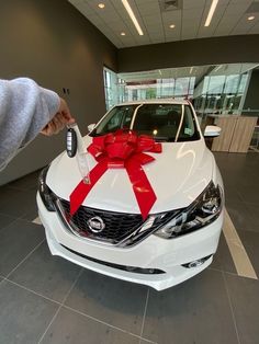 a white car with a red bow on it's hood is parked in a showroom