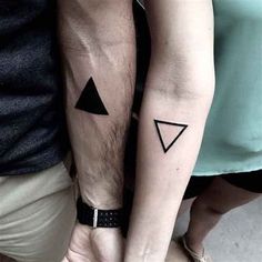 two people holding hands with tattoos on their arms and one has a black triangle in the middle