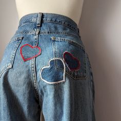 A mannequin wearing a pair of jeans with heart patches. Heart Pocket Pants, Unique Jeans Diy, Jean With Patches, Patchwork Baggy Jeans, Heart Embroidered Jeans, Jeans Decoration Ideas, Jeans Pocket Painting, Jean Patches Ideas, Patch On Jeans