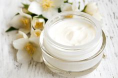 a jar of cream sitting on top of a wooden table next to white and yellow flowers