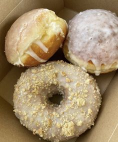 three donuts in a box with white frosting and sprinkled toppings