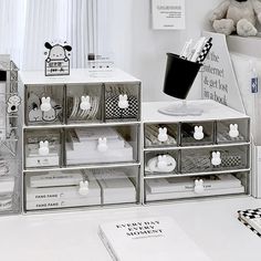 several clear boxes with various items in them on a white countertop next to a teddy bear