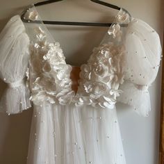 a dress hanging on a hanger with white flowers and pearls all over the top