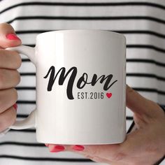 a woman holding a coffee mug with the word mom on it