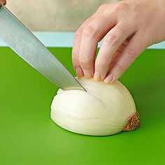 a person cutting onions with a knife on a green counter top next to a pair of scissors