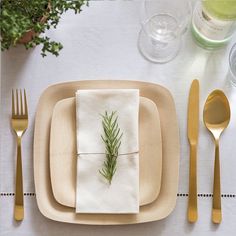 a place setting with silverware, napkins and green sprig on it