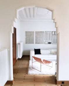 a living room with white furniture and wood floors in the center is seen through an archway