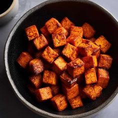 a bowl filled with cubed tofu next to a cup of coffee