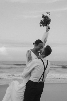 black and white photo of bride and groom kissing on the beach with ocean in background