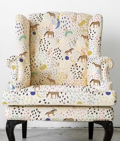 an upholstered chair with animal print on the back and arms, in front of a white wall