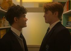 two young men standing next to each other in front of shelves with books on them